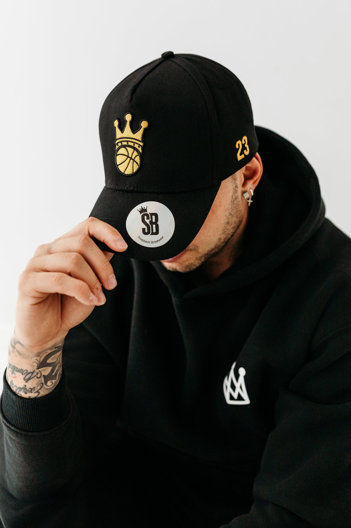 Model wearing Black Snapback hat with gold ball/crown logo 