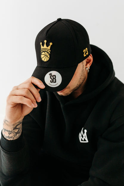 Model wearing Black Snapback hat with gold ball/crown logo 